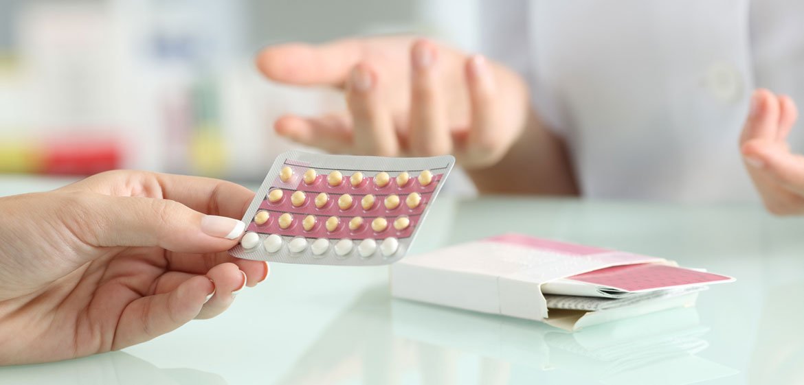 Eine Frau hält Pillen in einer Hand und eine Apothekerin erklärt etwas dazu.